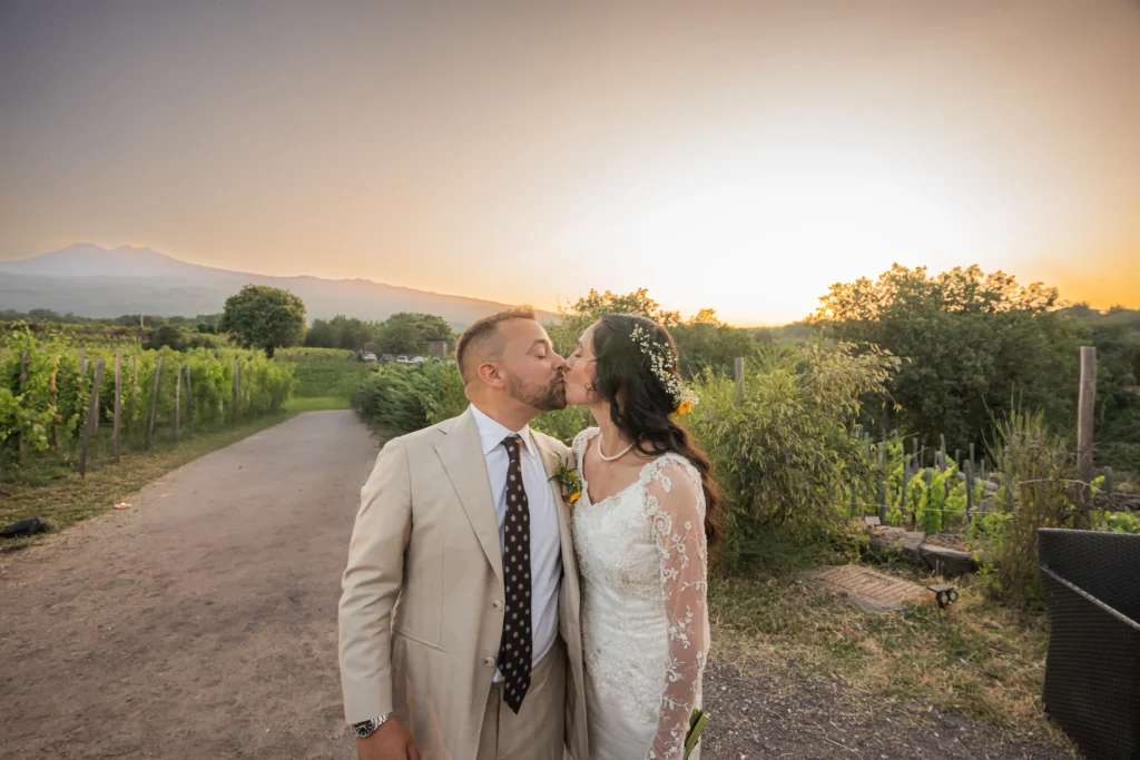 Bride and groom kissing at sunset in a Sicilian vineyard with Mount Etna views during a luxury wedding celebration.