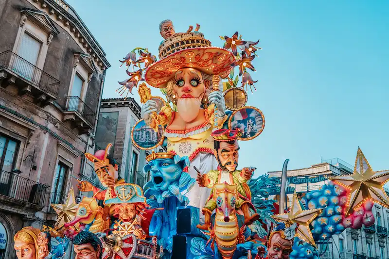 Colorful Sicilian carnival float with artistic masks and performers during a traditional cultural celebration in Sicily.
