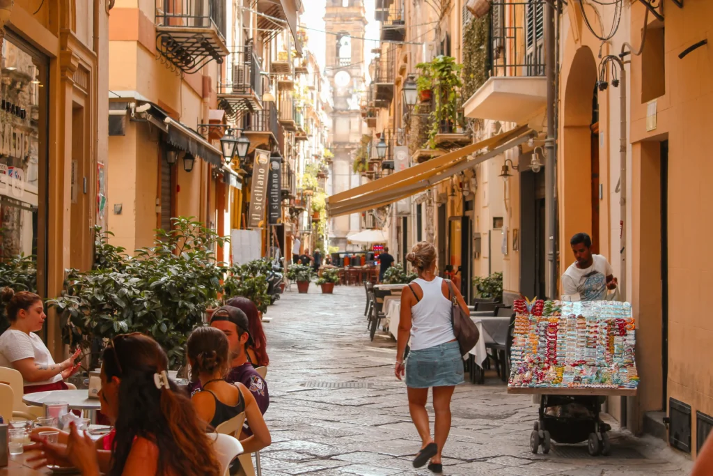 Charming historic street in Sicily with local cafés, traditional architecture, and people walking through a vibrant Sicilian town atmosphere.