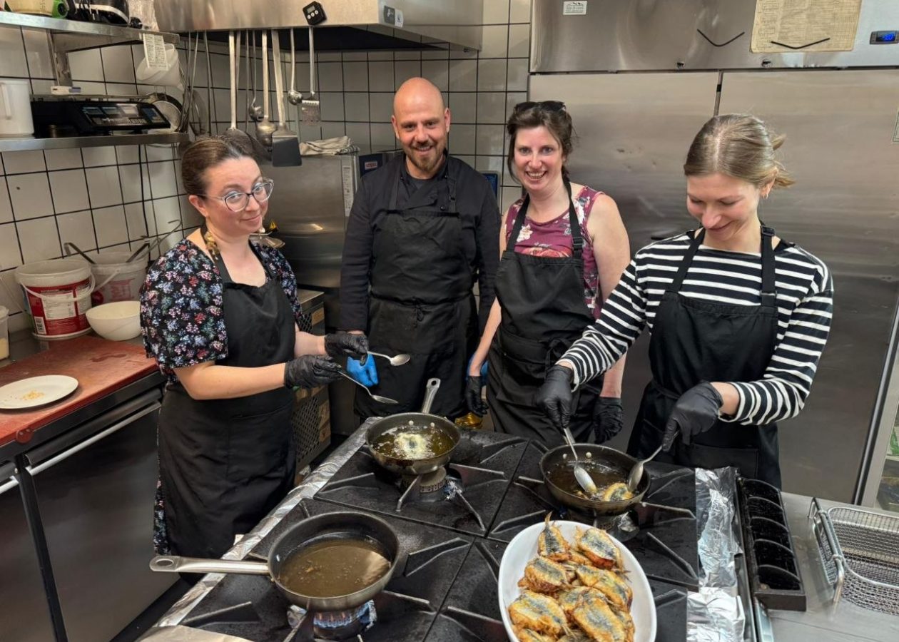 Tourists enjoying a hands-on Sicilian cooking class in a professional kitchen, preparing traditional local dishes during a culinary experience in Sicily.